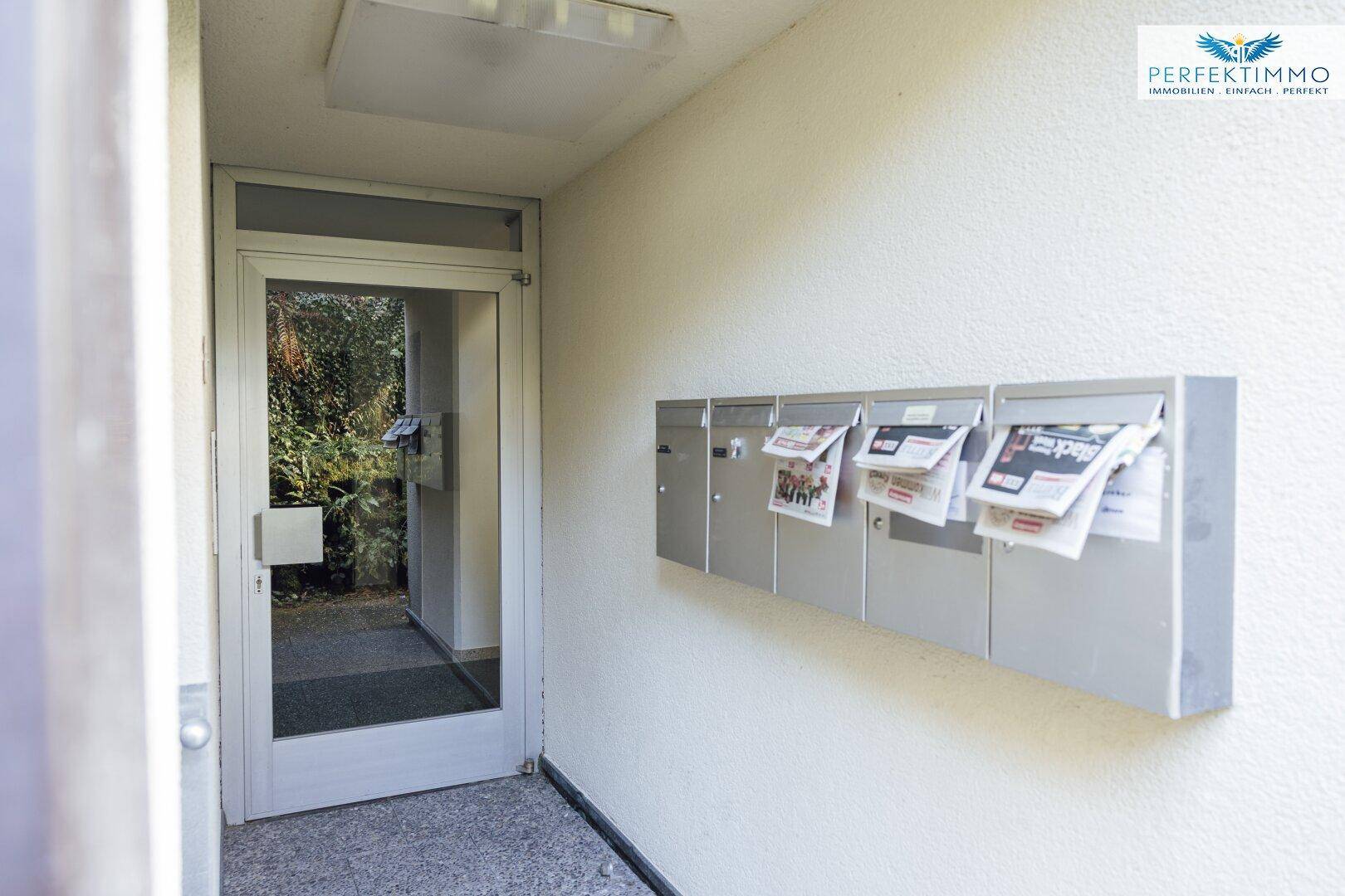 Eingangsbereich mit Briefkästen und einer Glastür, die ins Freie führt.