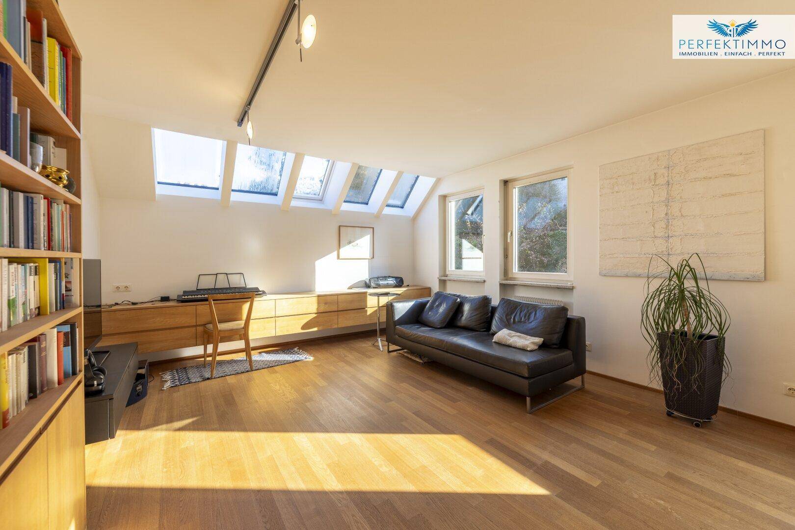 Sonniger Wohnbereich mit Holzboden, einem großen Bücherregal und dekorativen Pflanzen.