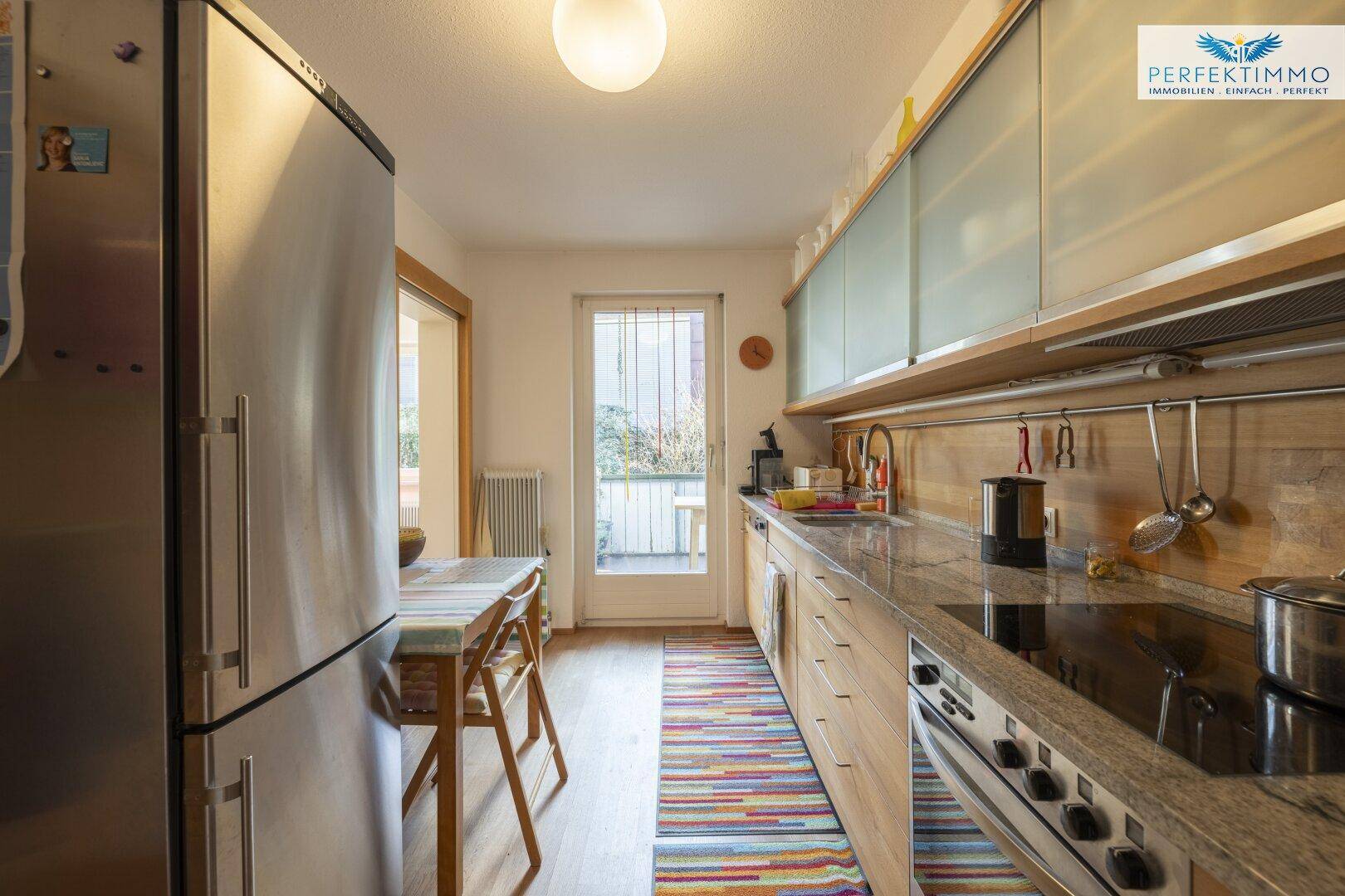 Helle Küche mit Induktionskochfeld, Backofen und Zugang zu einem kleinen Balkon.