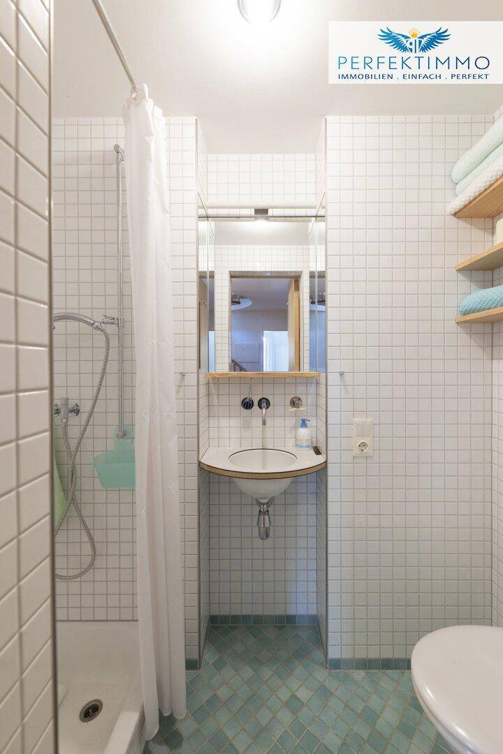 Kleines Badezimmer mit weißen Fliesen, Dusche, Waschbecken und WC, funktional eingerichtet.