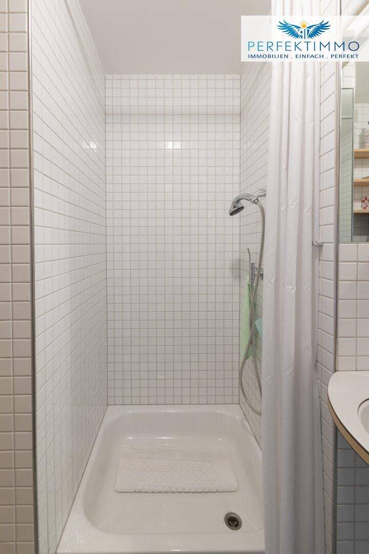 Duschbereich im Badezimmer mit weißen quadratischen Fliesen und Duschvorhang.