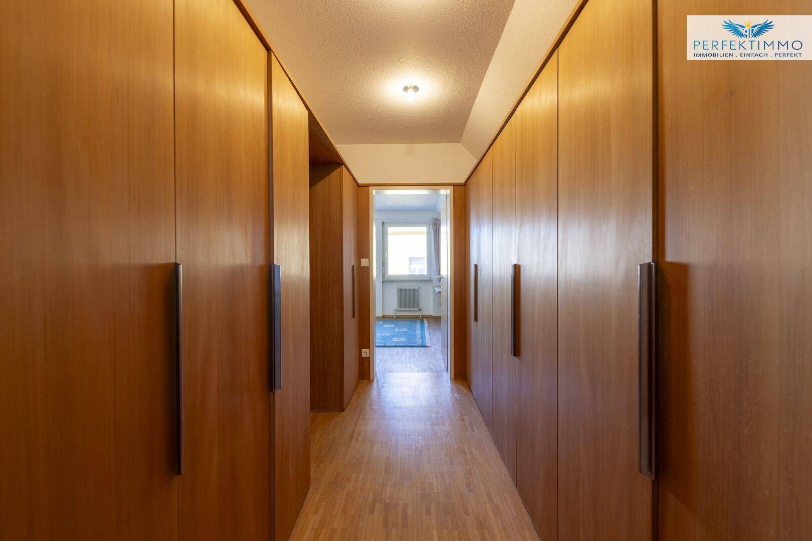 Langer Flur mit Einbauschränken und Holzboden, der zu einem weiteren Raum führt.
