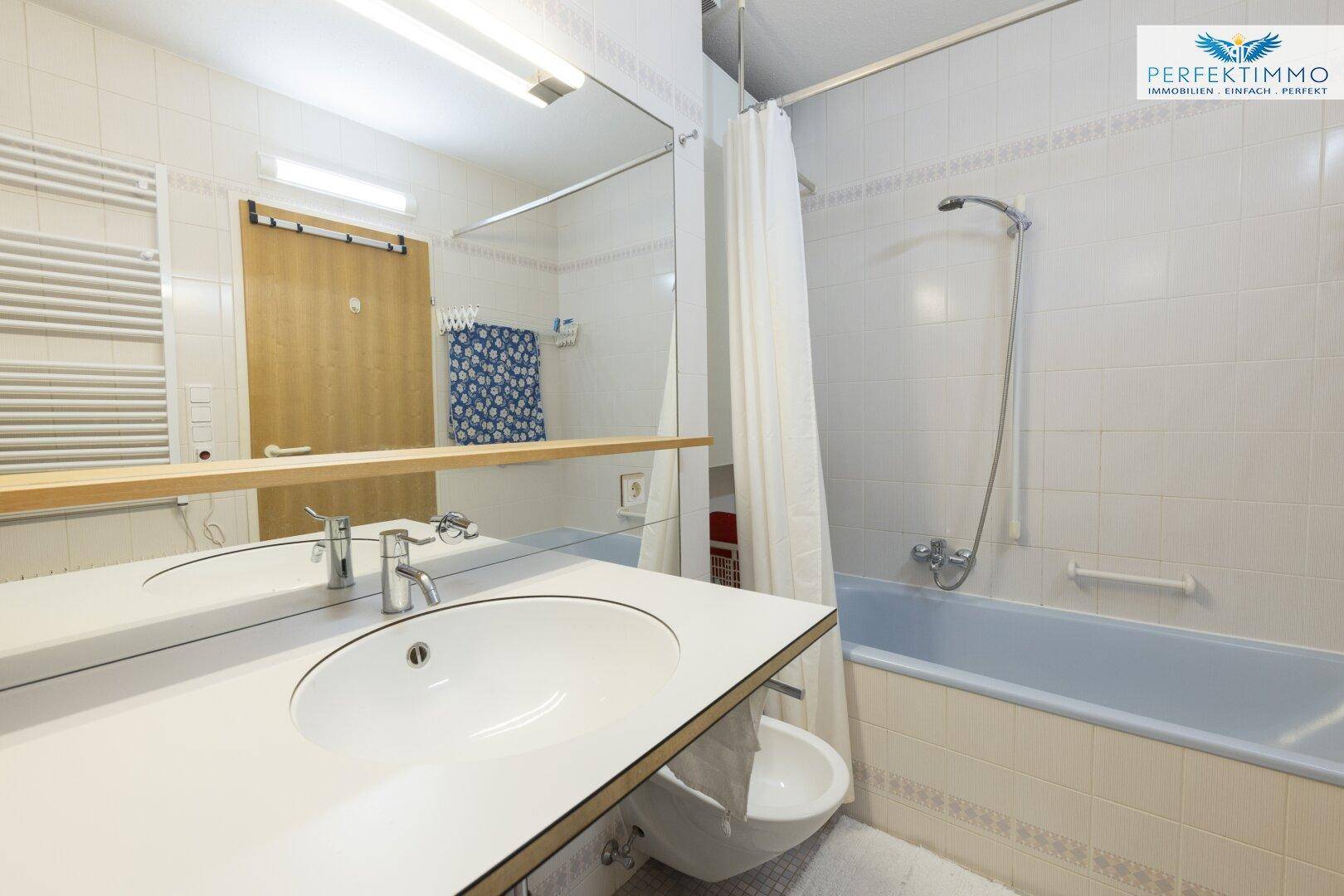 Badezimmer mit Badewanne, Einzelwaschbecken und großem Spiegel, gefliest.