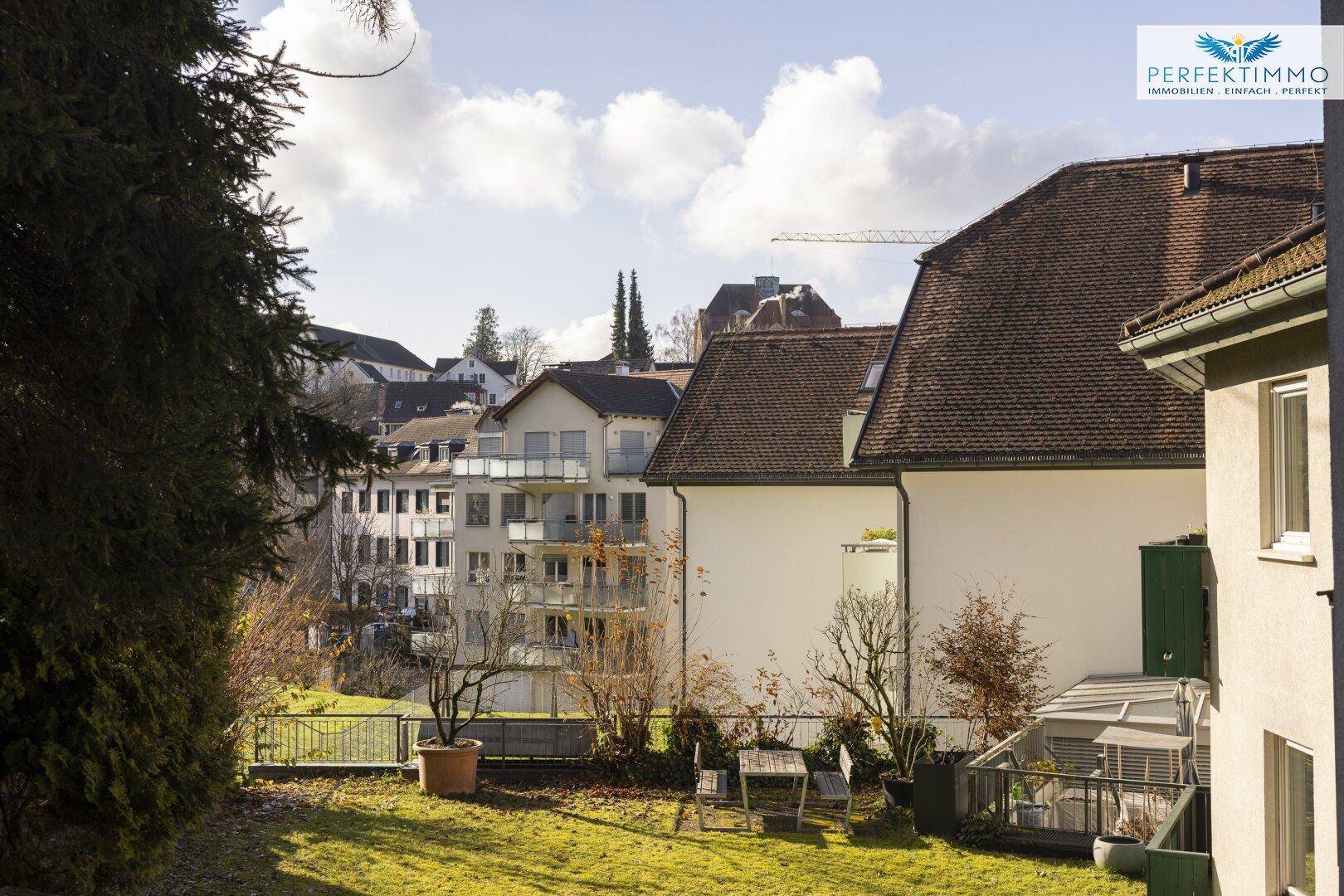 Sonniger Gartenbereich mit Rasenfläche und Sitzgelegenheiten, umgeben von Bäumen.