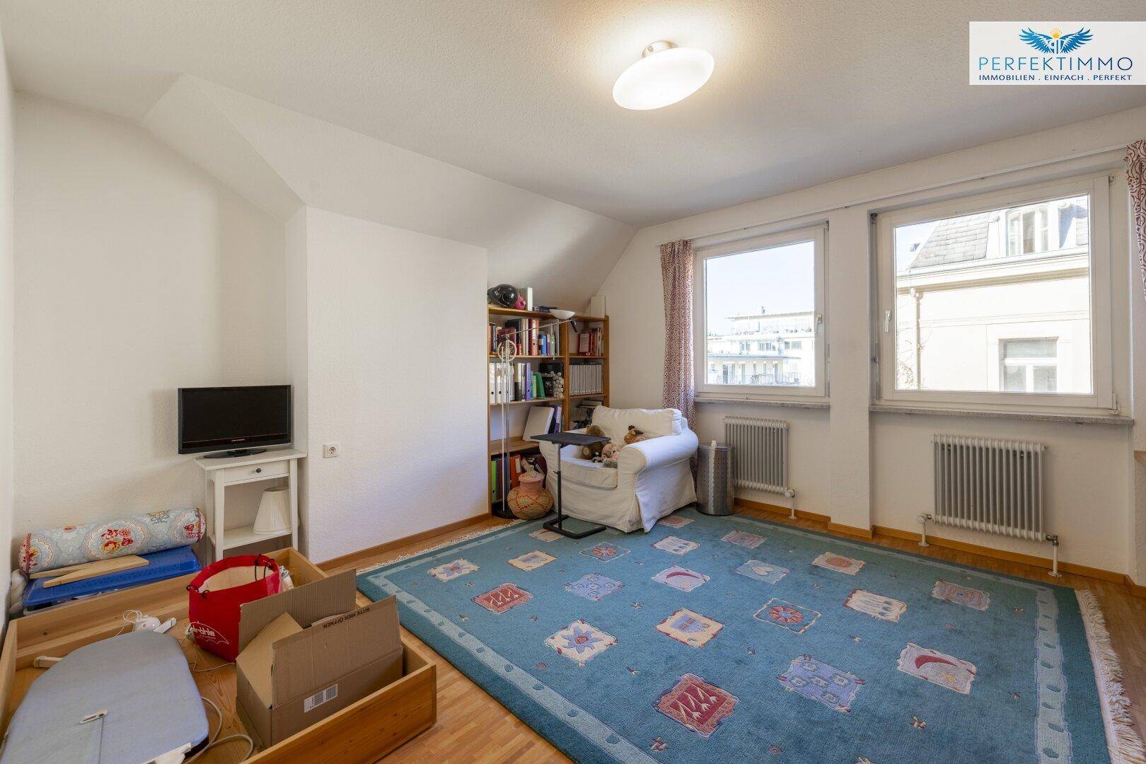 Gemütliches Schlafzimmer mit Dachschräge, Holzboden und zwei Fenstern.