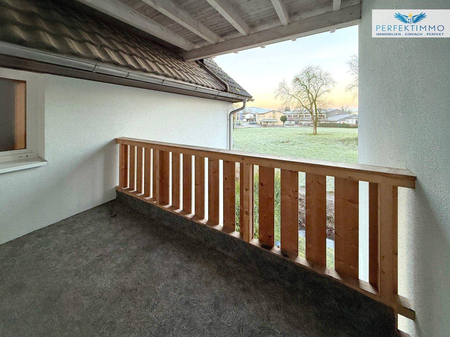 Überdachter Balkon mit Holzgeländer und Blick auf die grüne Umgebung.