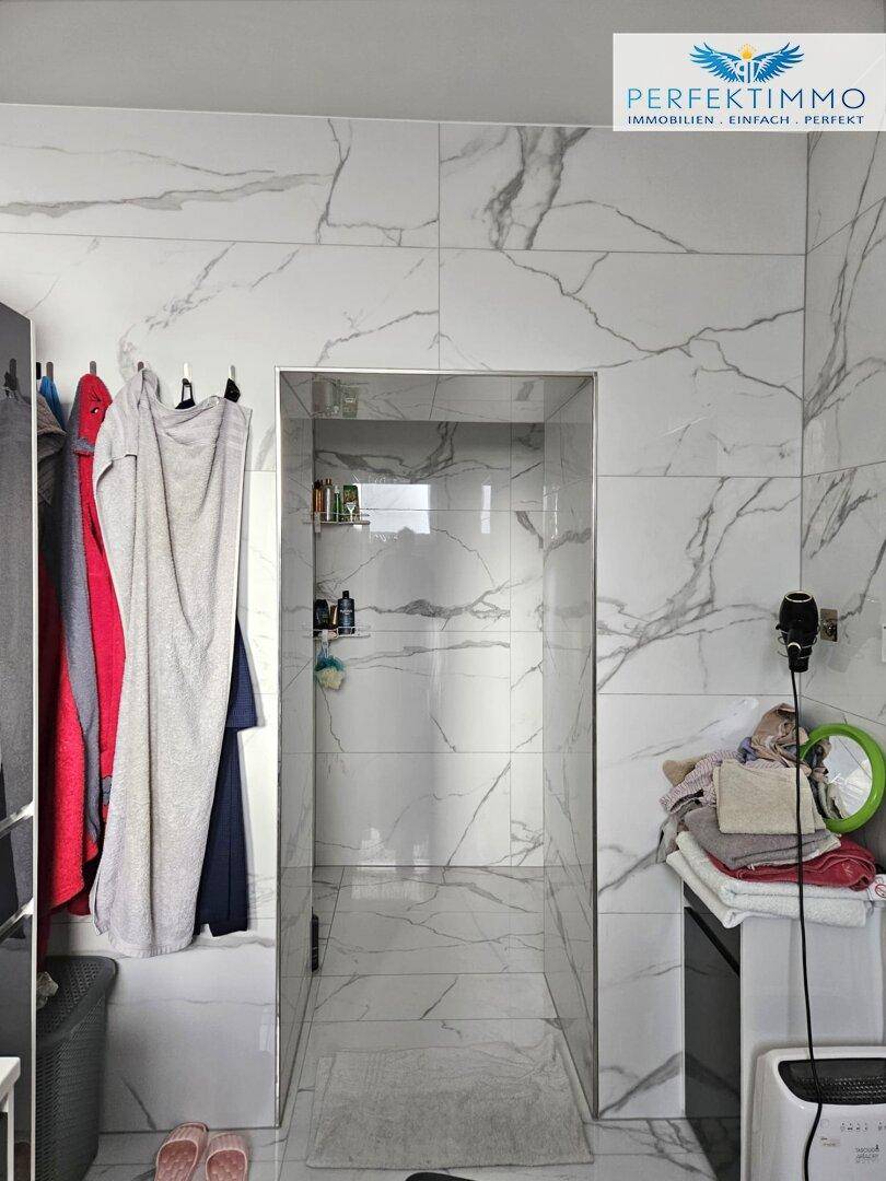 Modernes Badezimmer mit großformatigen Marmorfliesen und offener Duschkabine.