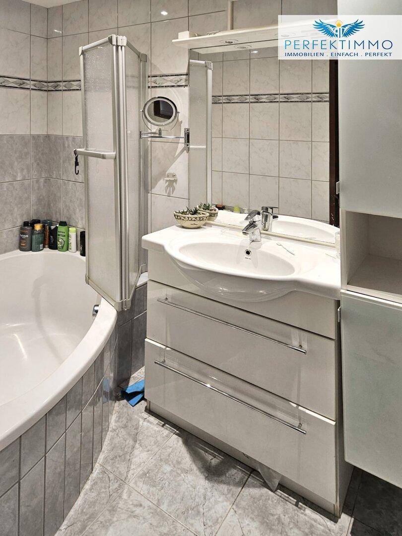 Helles Badezimmer mit Badewanne, Einzelwaschbecken und hellgrauen Fliesen.