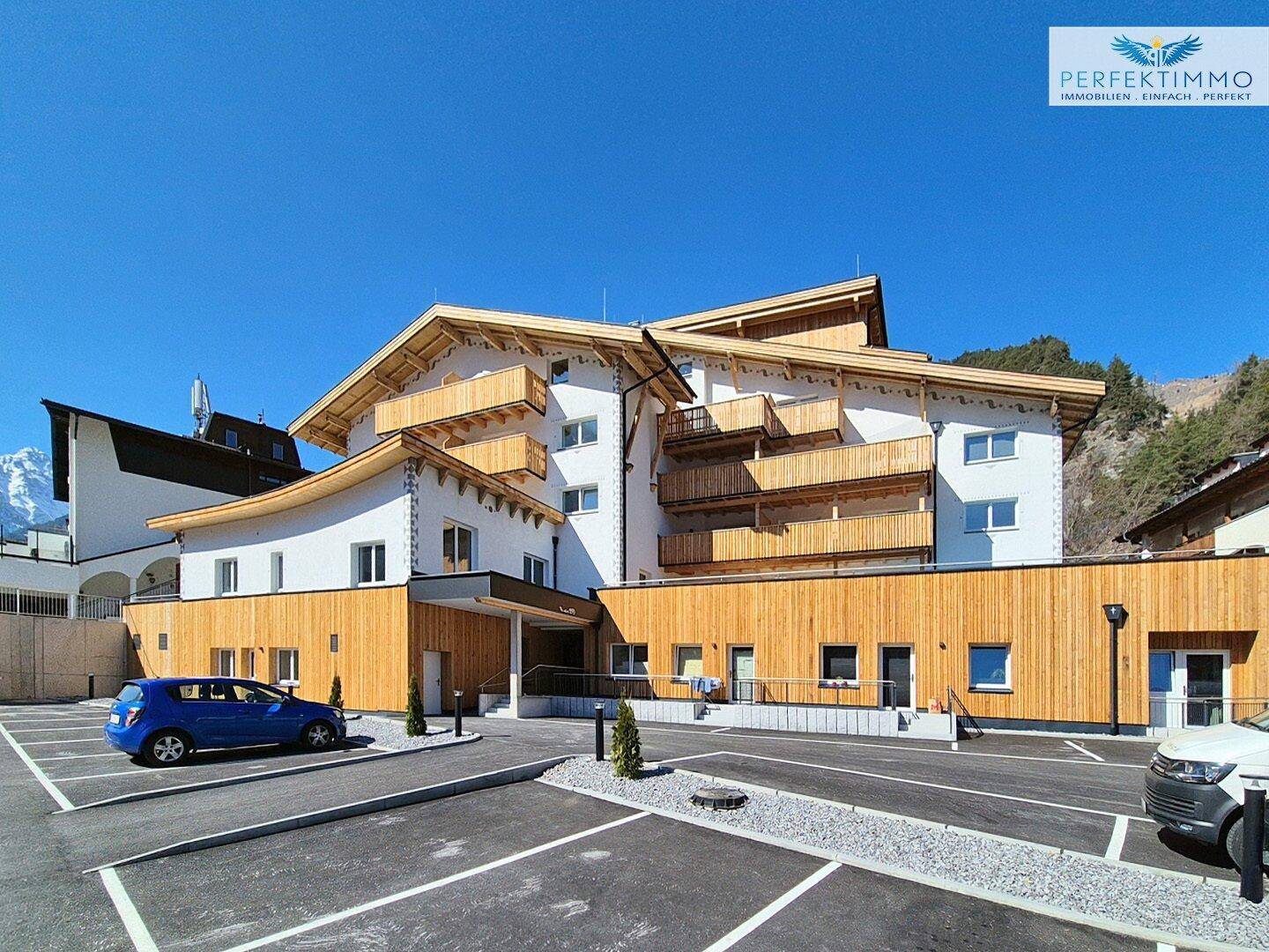 Modernes Mehrfamilienhaus mit Holzfassade und ausreichend Parkplätzen im Freien.