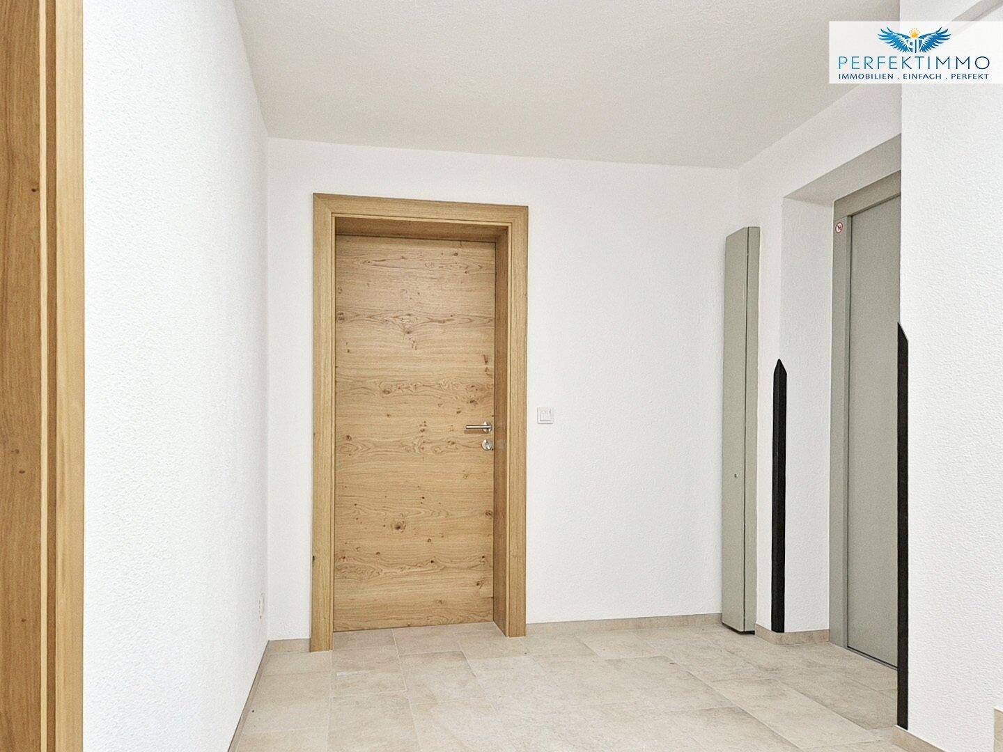 Heller Flur mit Fliesenboden und Holztür, inklusive Zugang zu einem modernen Aufzug.