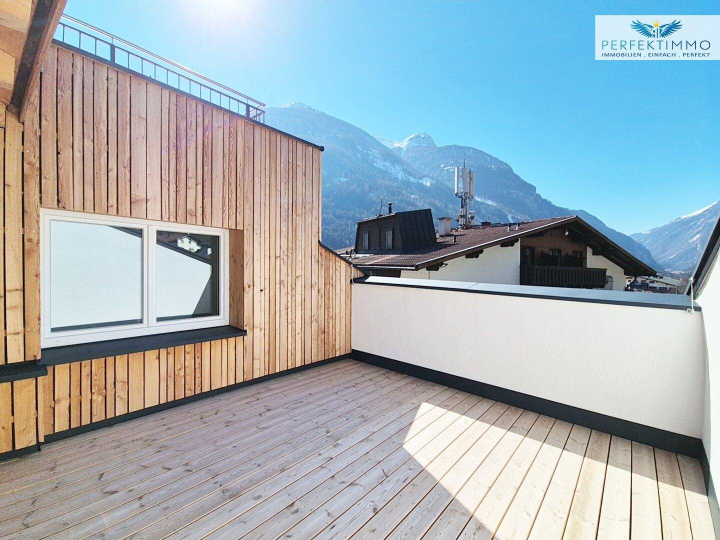 Große Holzterrasse mit Bergblick, umgeben von moderner Holzfassade.