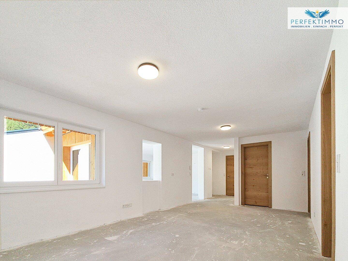 Unfertiger Innenraum mit weißen Wänden und Rohbetonboden, bereit für den weiteren Ausbau.