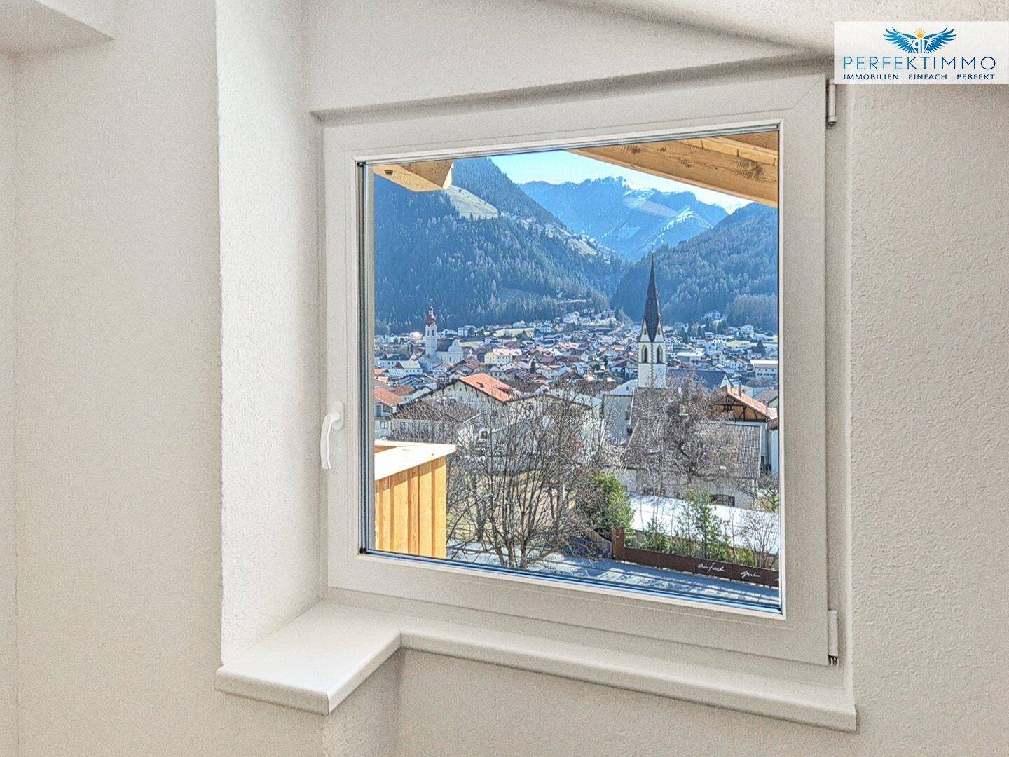 Fenster mit weitem Blick auf ein malerisches Dorf und die umliegende Berglandschaft.