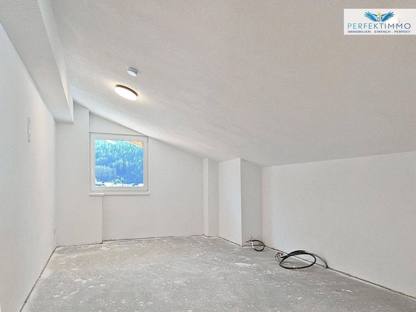 Unfertiger Raum im Dachgeschoss mit schräger Decke und Fenster, bereit für den Ausbau.