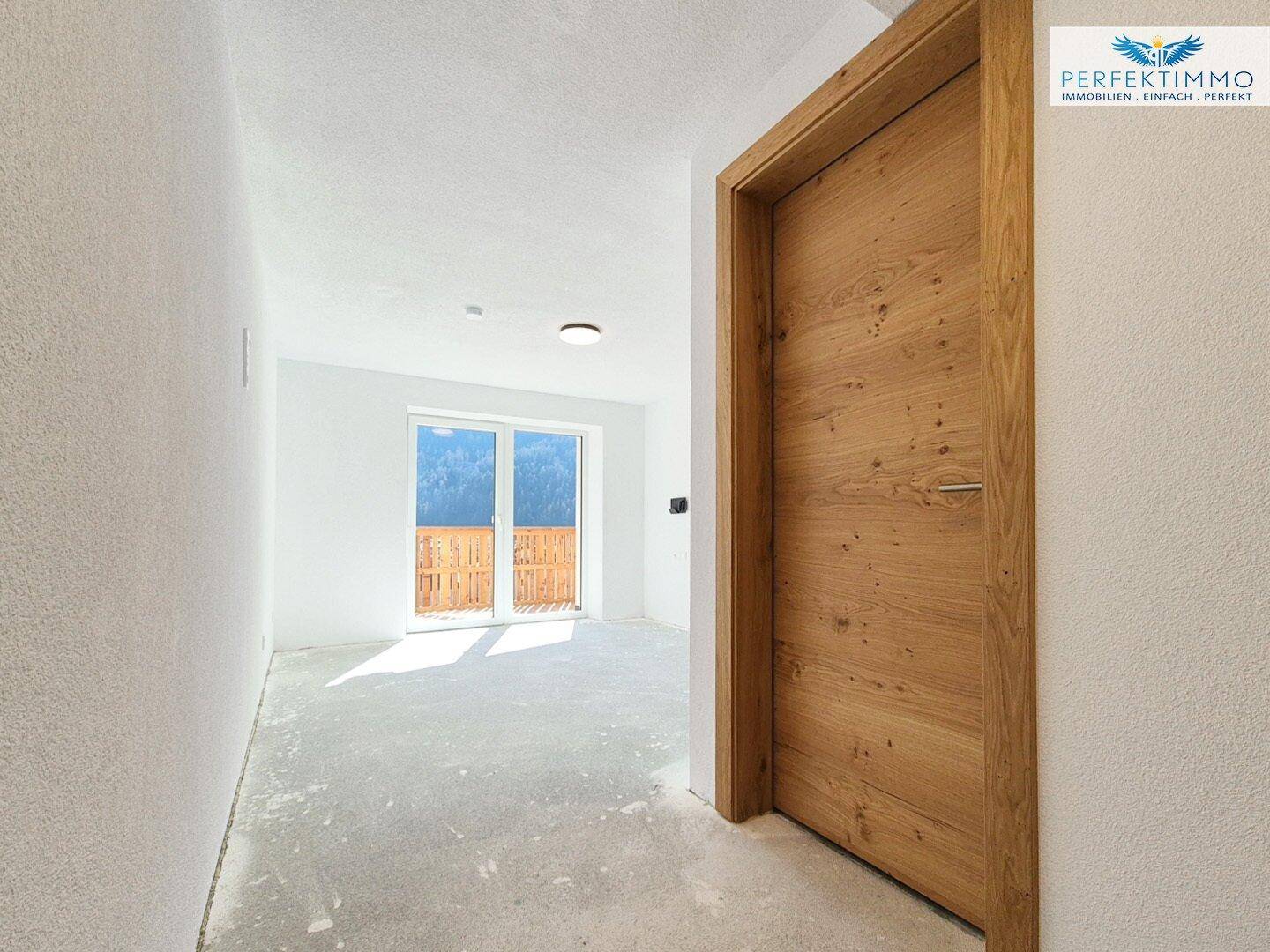Heller Flur mit Holztür und Blick auf einen Raum mit Balkonzugang.
