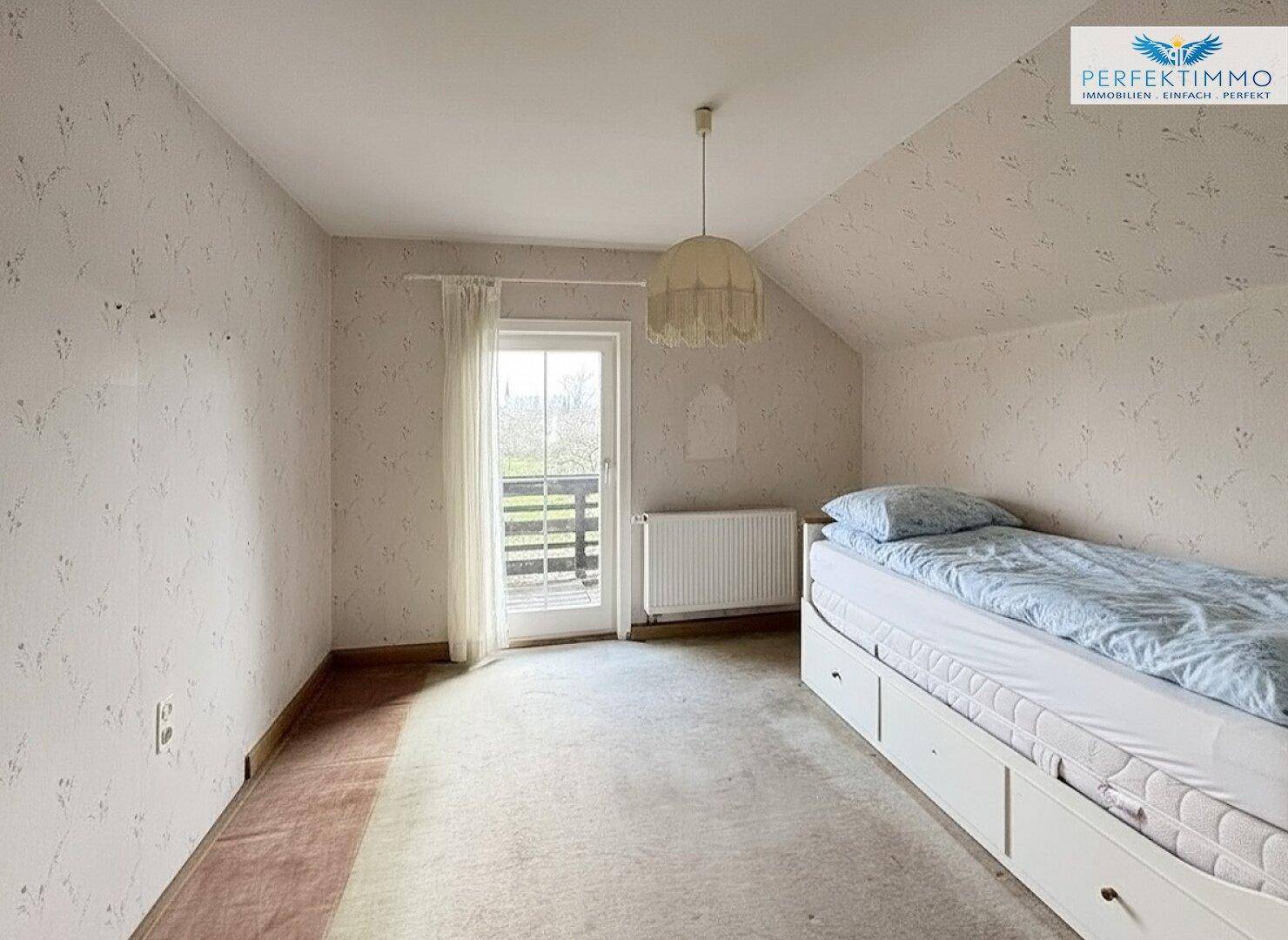Helles Schlafzimmer mit Dachschräge, Teppichboden und Zugang zu einem Balkon.