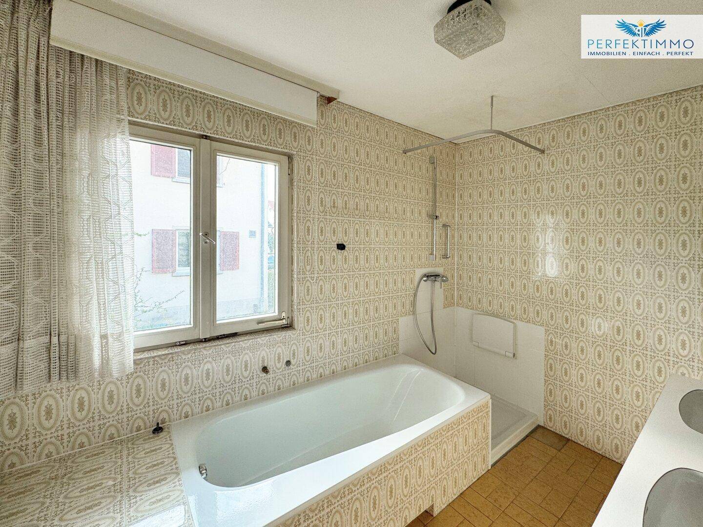 Badezimmer im 80er-Jahre-Stil mit Badewanne, gemusterten Fliesen und Fenster.