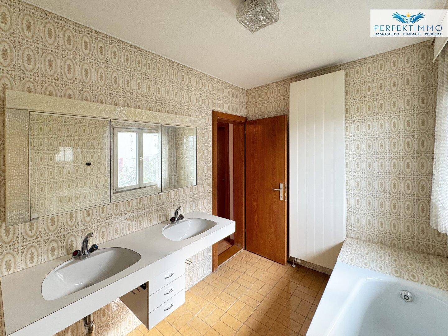 Geräumiges Badezimmer im 80er-Jahre-Stil mit Doppelwaschbecken, Badewanne und gemusterten Fliesen.