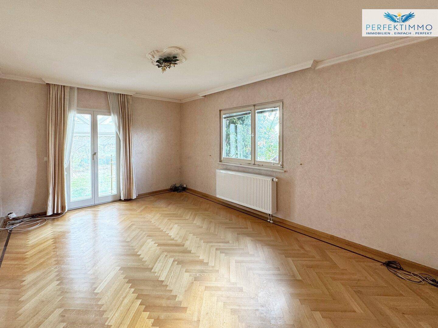 Helles Wohnzimmer mit Fischgrätparkett, Zugang zur Terrasse und großen Fenstern.