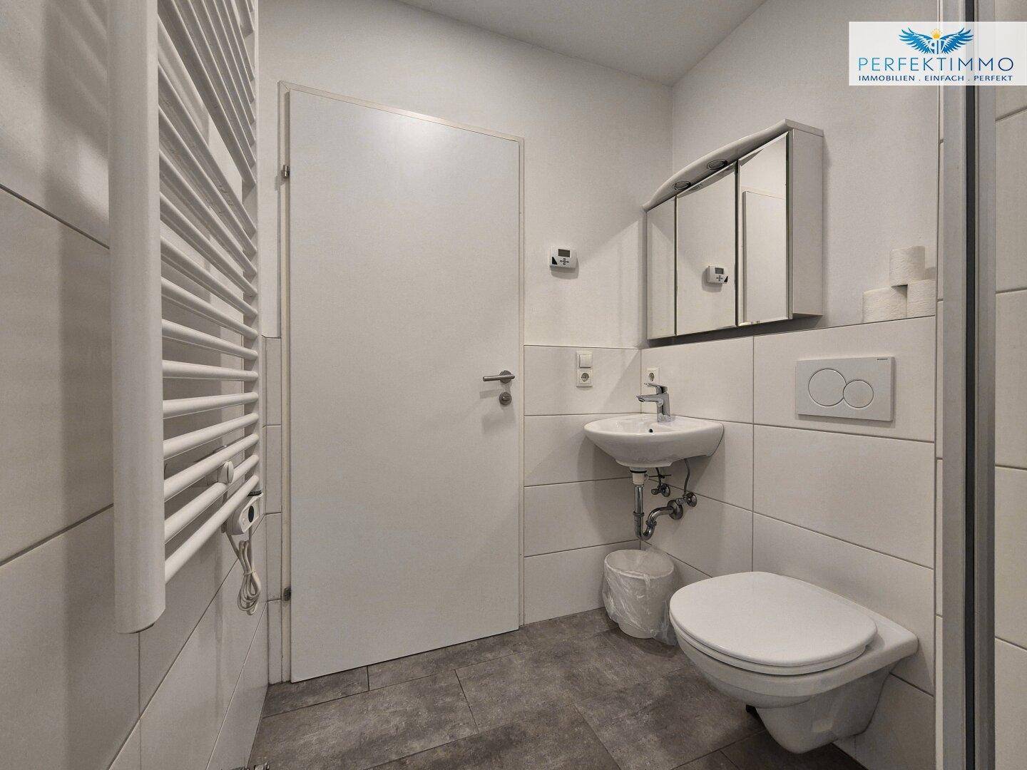 Helles Badezimmer mit Waschbecken, WC und praktischem beheiztem Handtuchhalter.