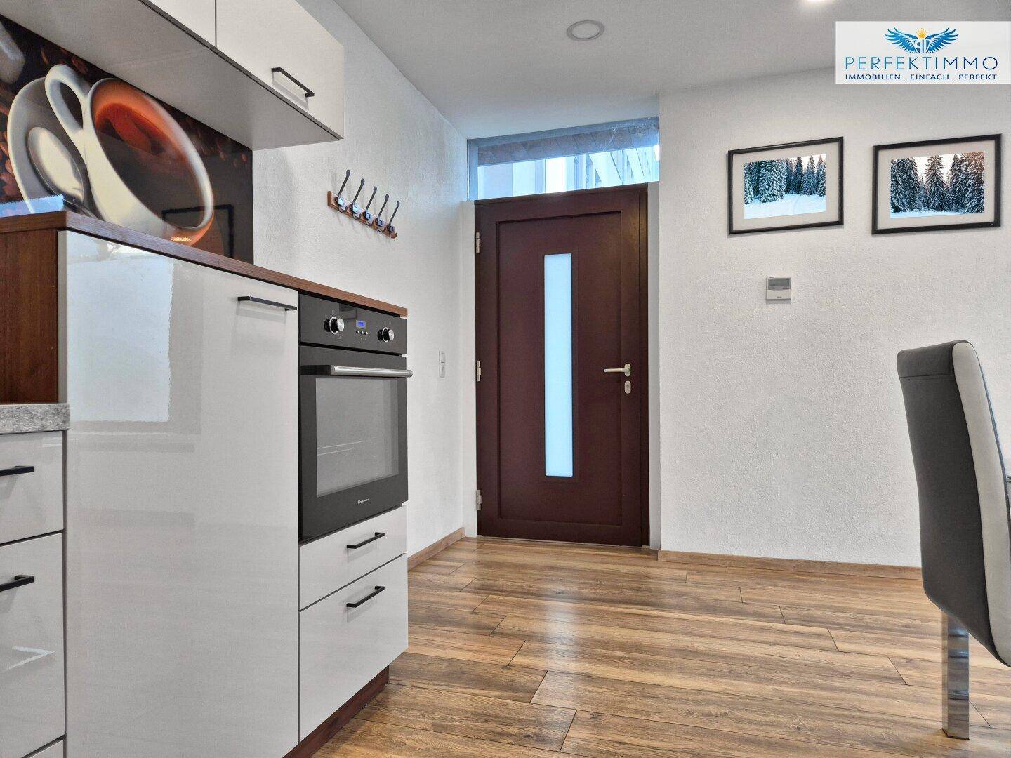 Heller Eingangsbereich mit Holzboden und moderner Tür, angrenzend an die Küche.