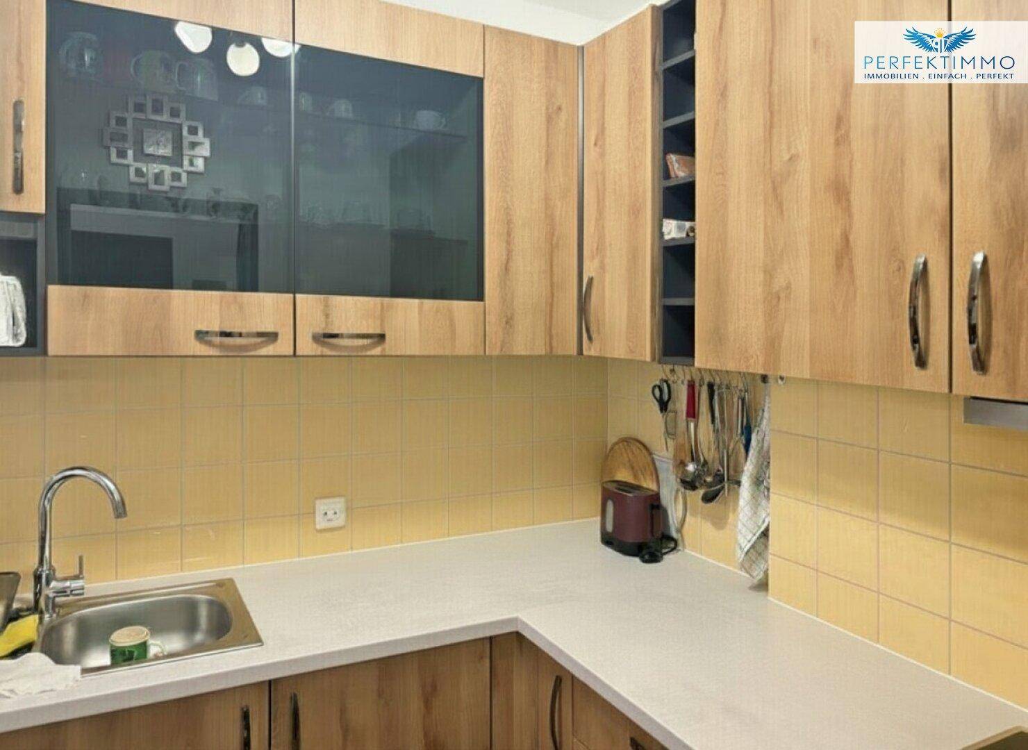 Funktionale Küche mit Holzschränken, Spüle und gelben Fliesen als Spritzschutz, praktisch und hell.