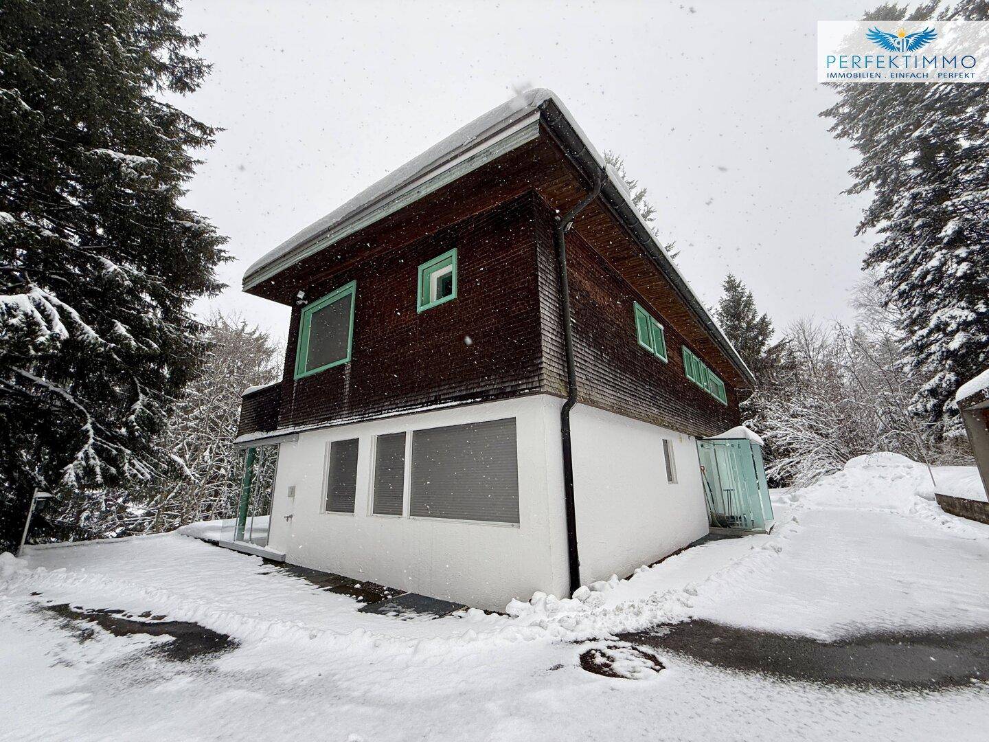 Charmantes Haus mit Holzfassade und weißem Sockel, eingebettet in eine verschneite Winterlandschaft.