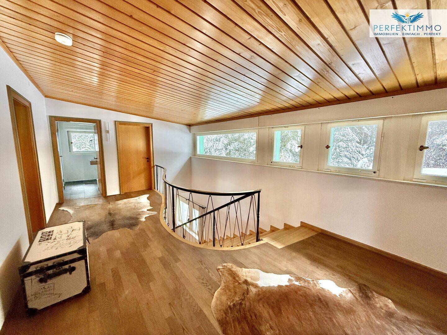 Heller Flur im Obergeschoss mit Holzboden und Holzdecke, der zu weiteren Räumen führt.