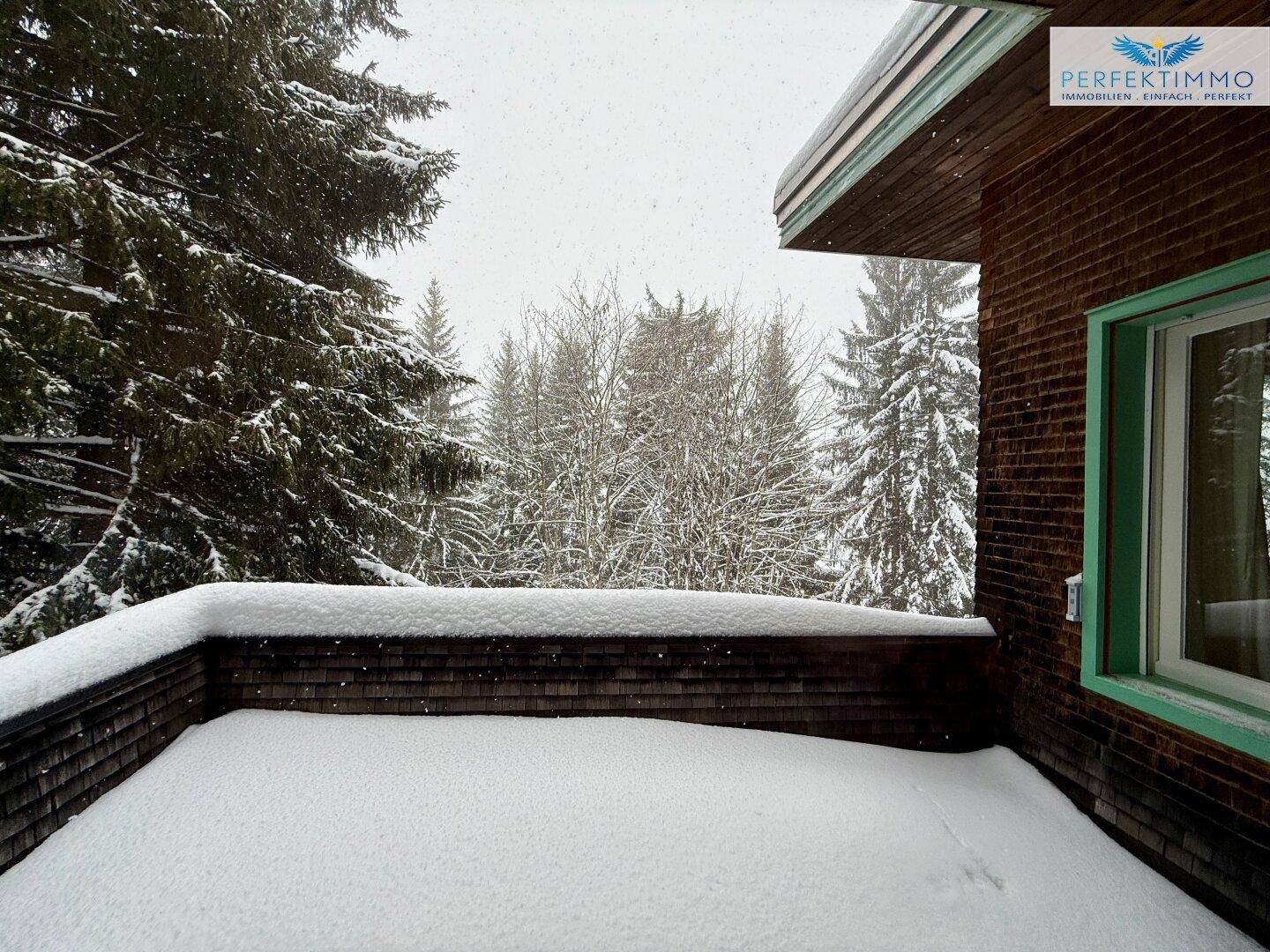 Balkon im Winter, bedeckt mit Schnee, bietet einen weiten Blick auf die umliegenden verschneiten Bäume.