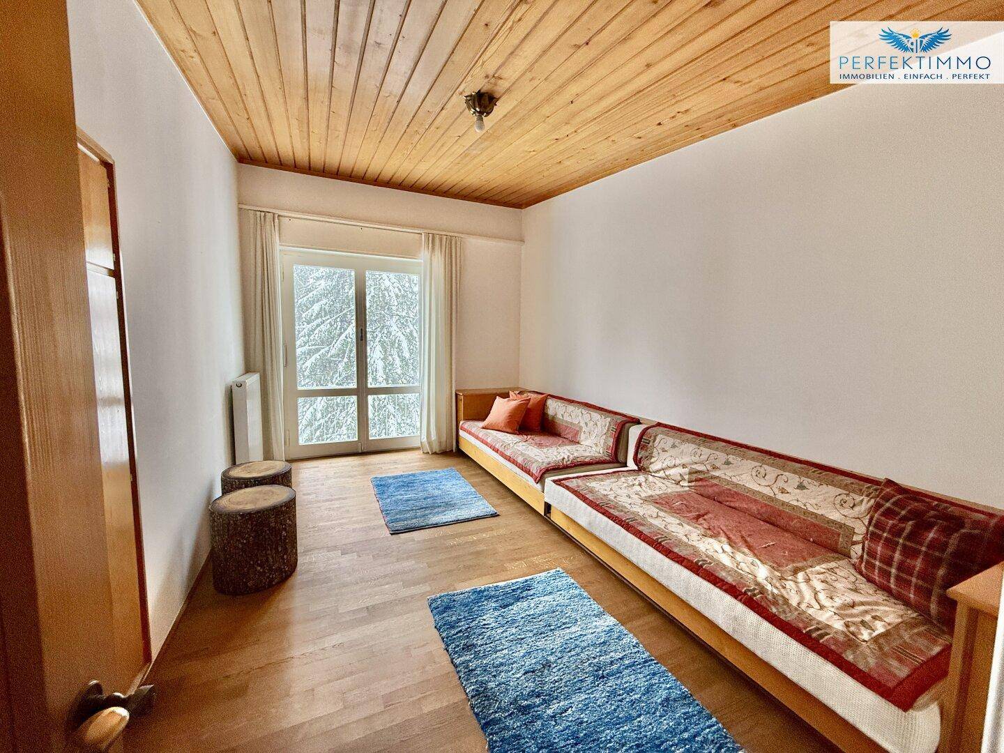 Gemütliches Schlafzimmer mit Holzboden und Holzdecke, ausgestattet mit einer langen Sitzbank und Balkonzugang.