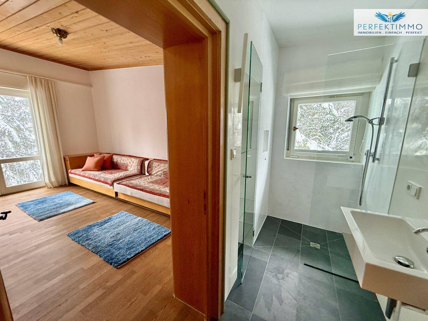 Schlafzimmer mit Holzboden und Zugang zu einem modernen Duschbad mit Glaswänden.