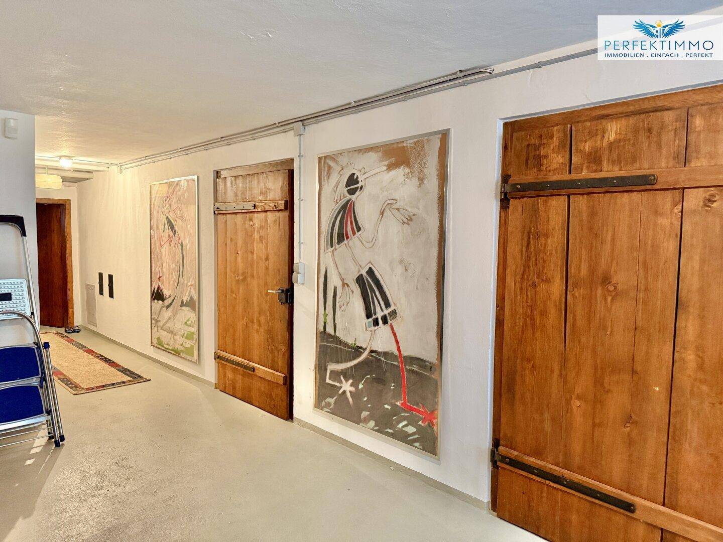 Kellerflur mit Holztüren und Kunstwerken an den Wänden, bietet Zugang zu verschiedenen Räumen.