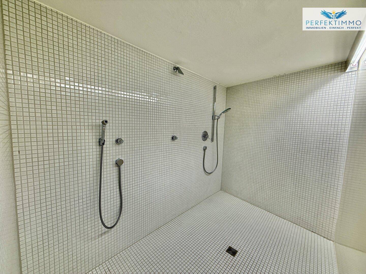 Großer Duschbereich mit weißen Mosaikfliesen und zwei Duschköpfen, modern und funktional.