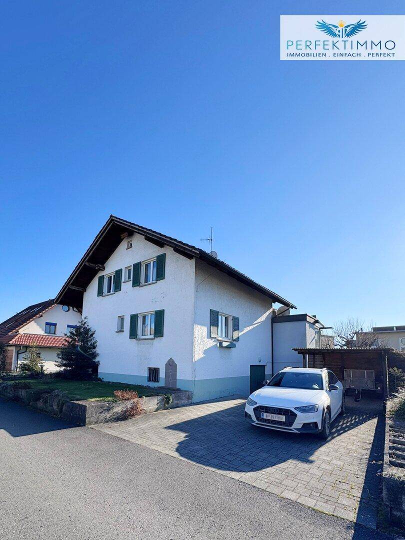 Vorderansicht des Hauses mit Einfahrt und geparktem Auto an einem sonnigen Tag.