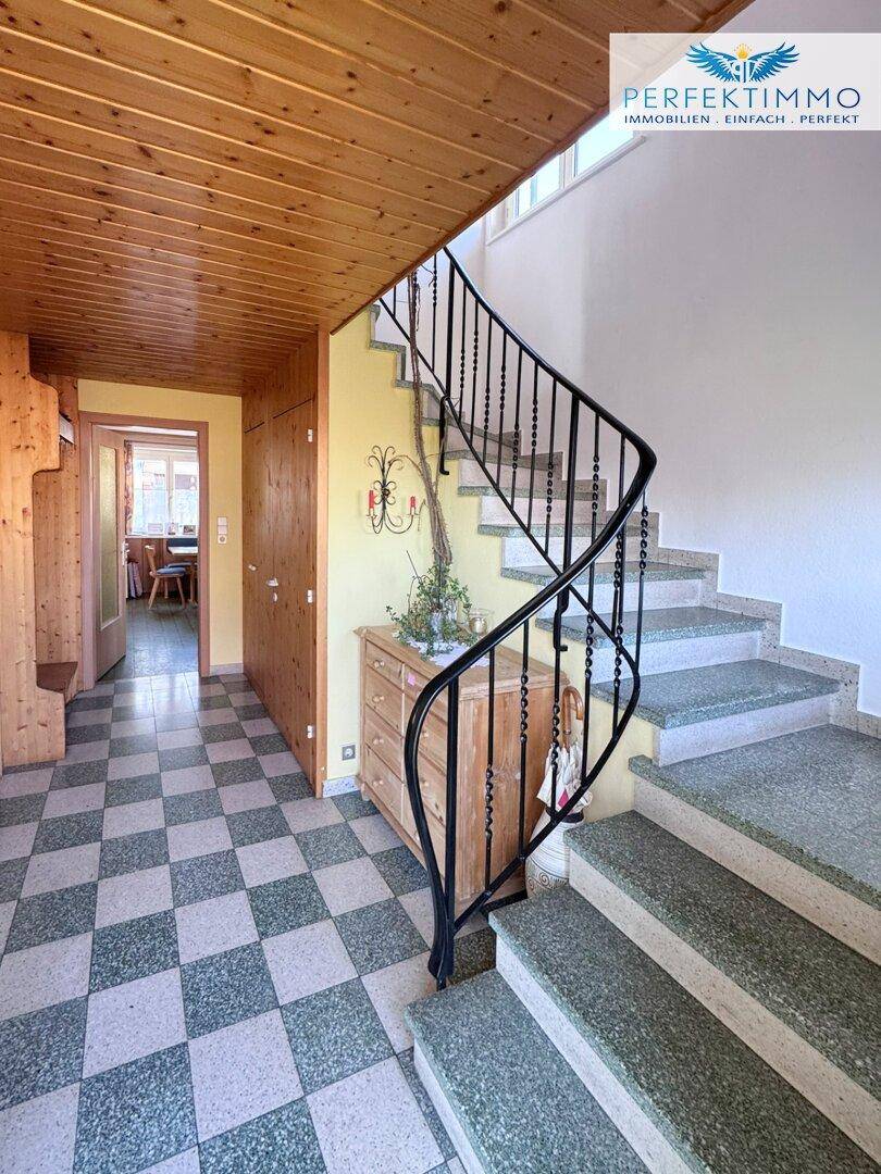 Heller Eingangsbereich mit geschwungener Treppe und Holzdecke.