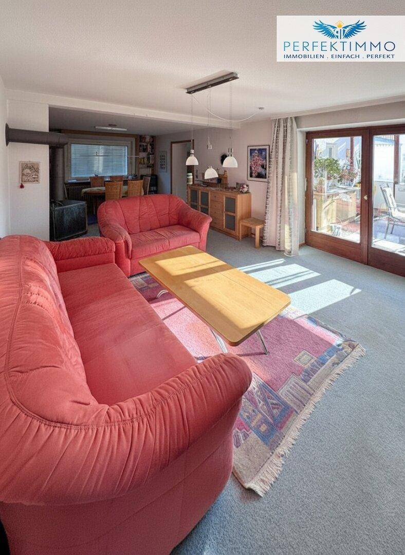 Geräumiges Wohnzimmer mit Teppichboden, Zugang zur Terrasse und Essbereich im Hintergrund.