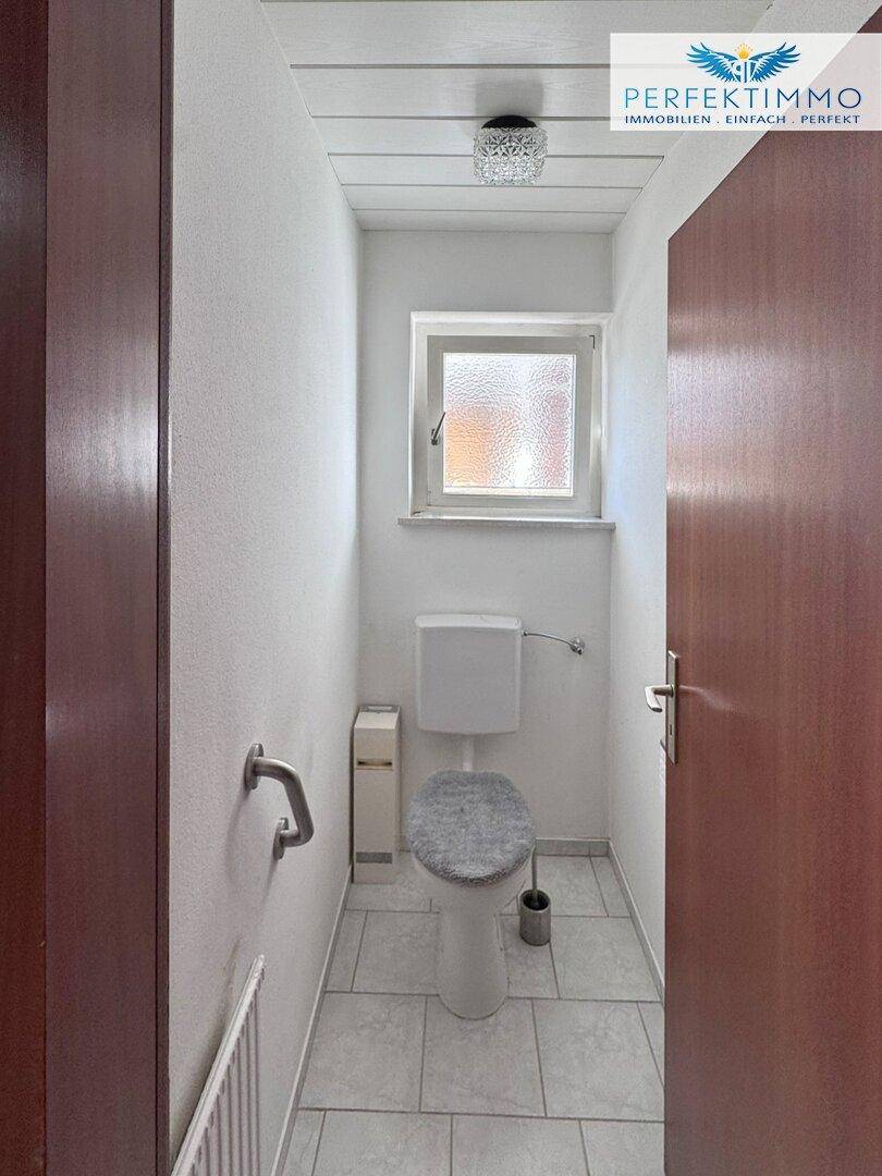 Kleines Gäste-WC mit Fenster, Fliesenboden und Wandhaltegriff.