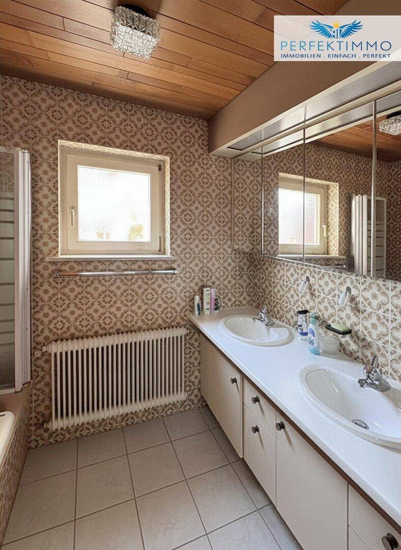 Badezimmer mit Doppelwaschbecken, Spiegelschrank und gemusterten Fliesen.