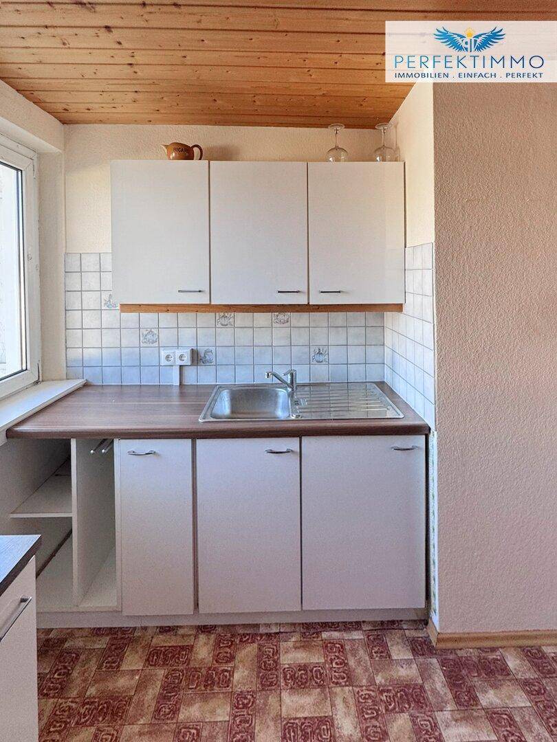 Kleine Küchenzeile mit Spüle, Oberschränken und Holzdecke.
