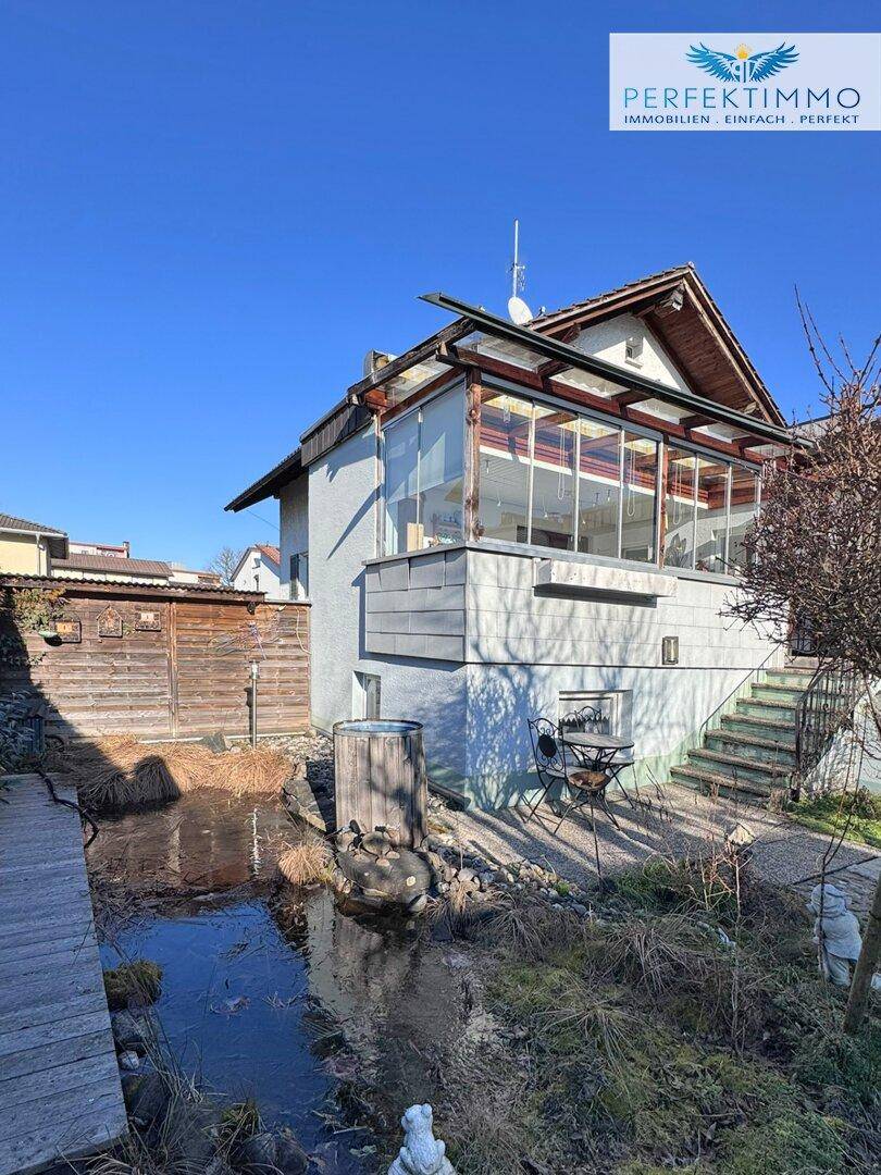 Rückseite des Hauses mit Wintergarten, Teich und kleiner Terrasse im Garten.