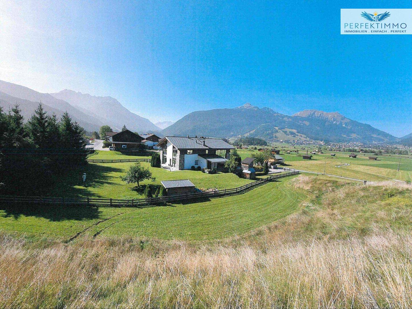 Luftaufnahme eines Einfamilienhauses in einer grünen Tallandschaft mit Bergblick.