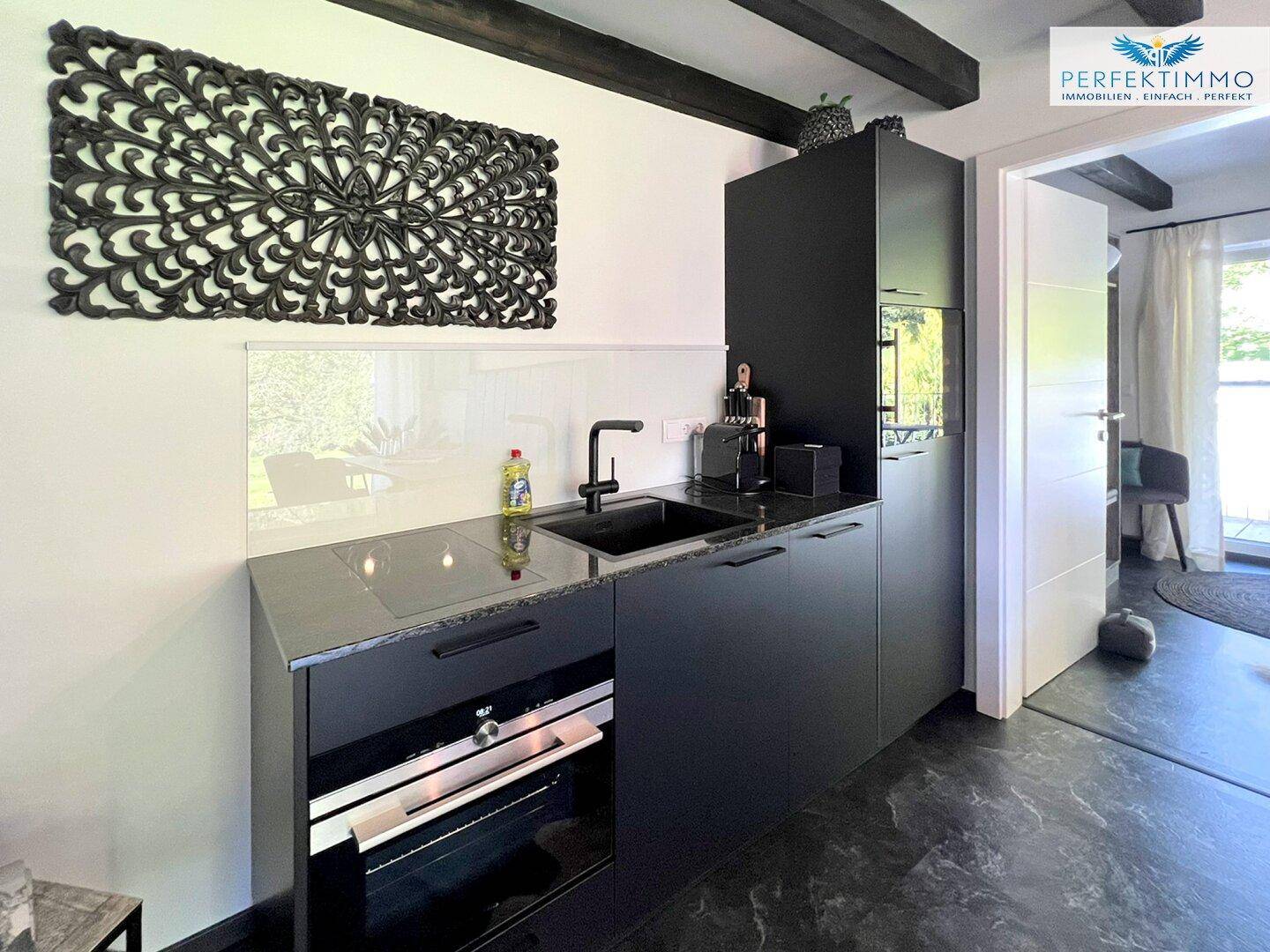 Moderne Küchenzeile in Schwarz mit integriertem Backofen und Arbeitsplatte aus Granit.