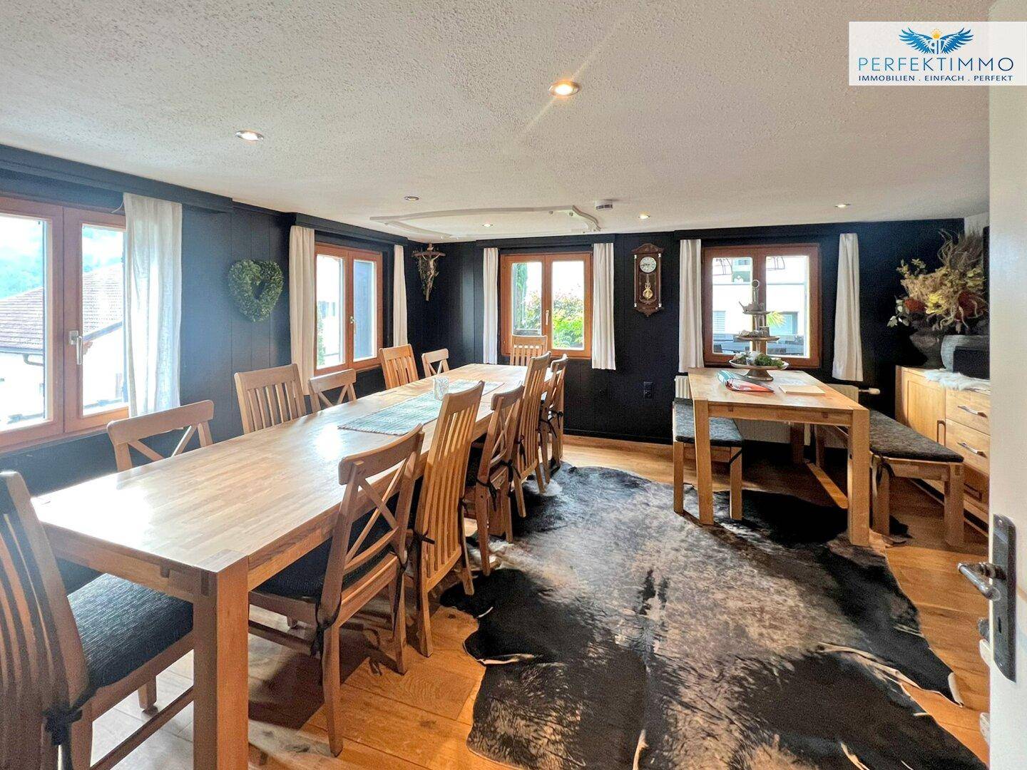 Großer Essbereich mit Holztischen, Stühlen und rustikalem Teppich.