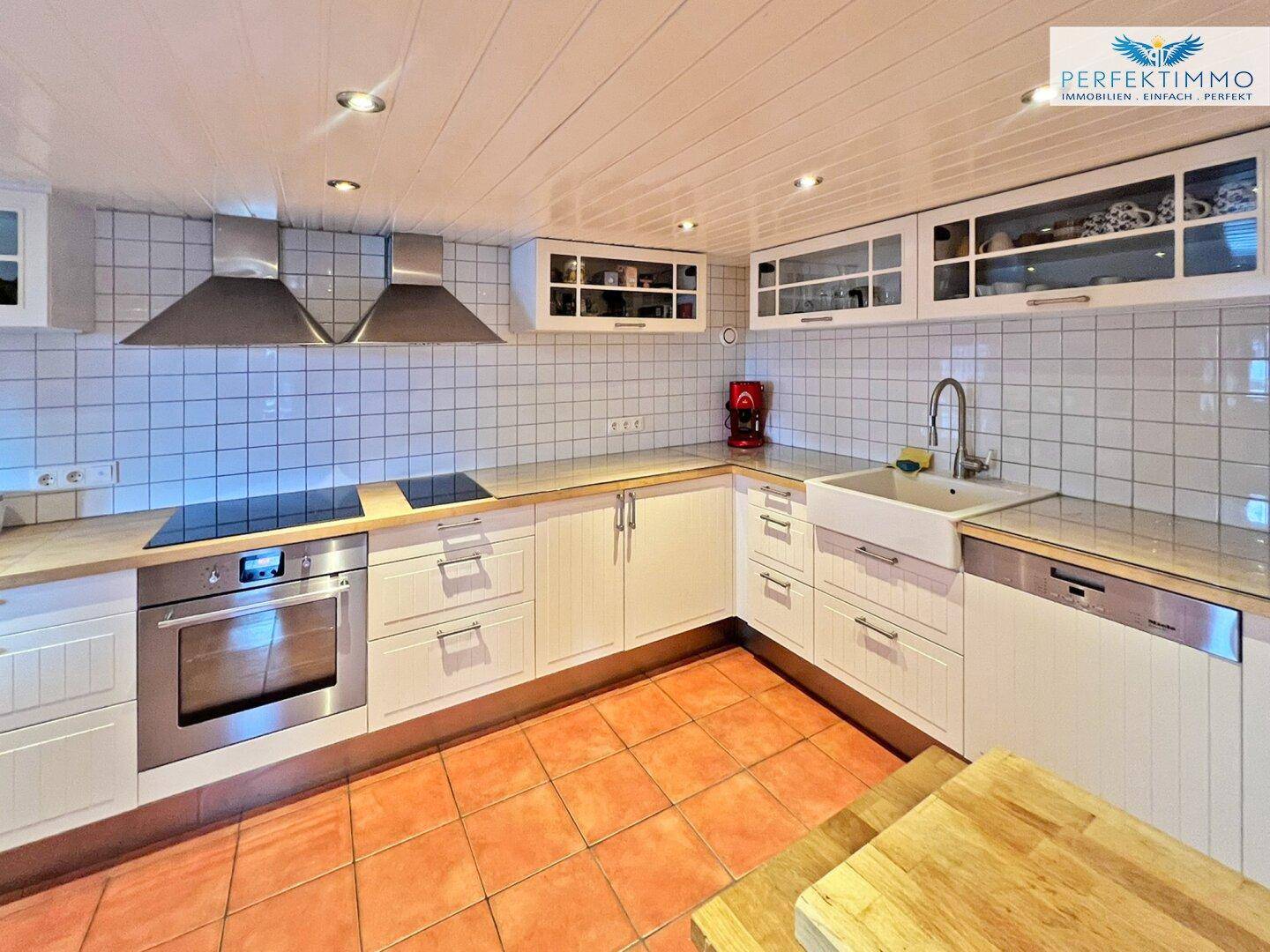 Helle Küche mit weißen Schränken, Holz-Arbeitsplatten und Fliesenboden.
