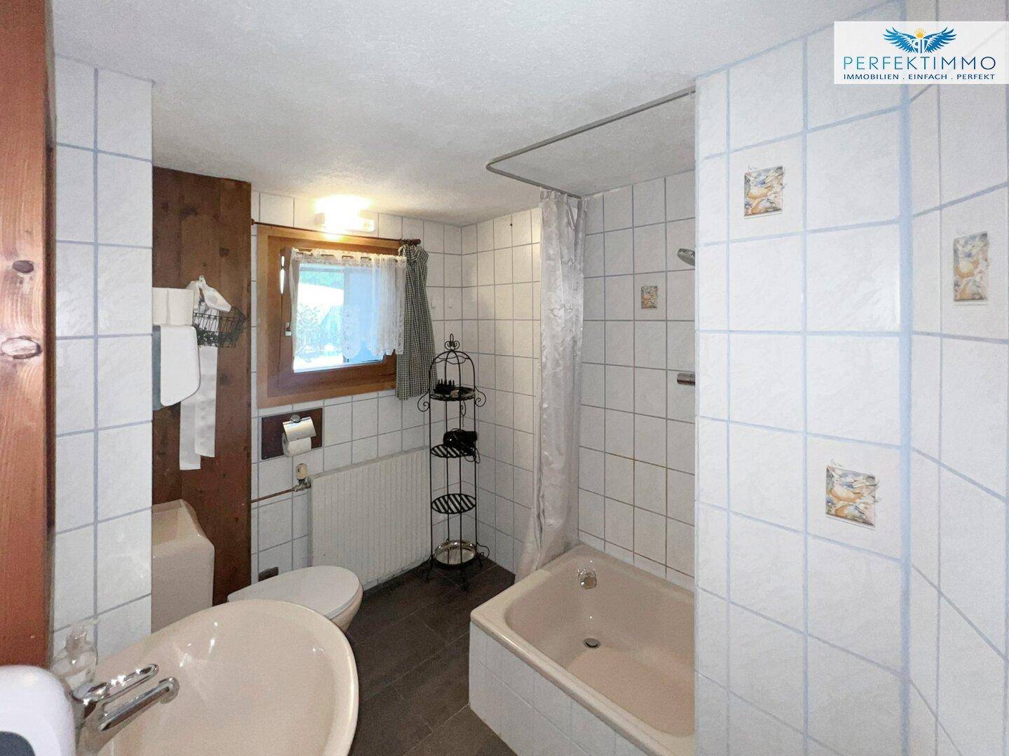Badezimmer mit Badewanne, Dusche, weißen Fliesen und Fenster.