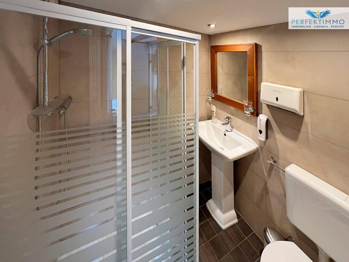 Modernes Badezimmer mit Duschkabine, Waschtisch und braunen Fliesen.