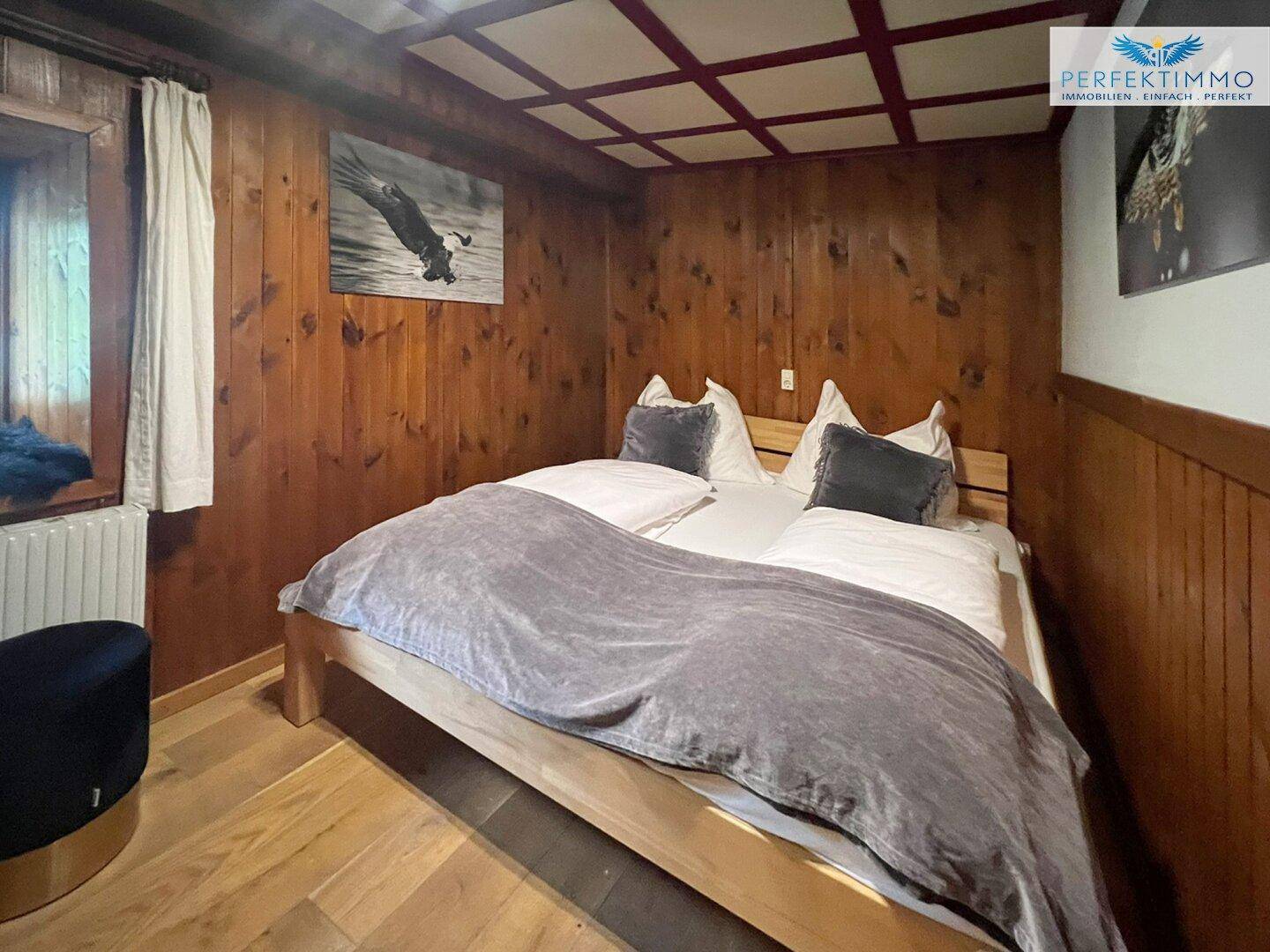 Rustikales Schlafzimmer mit Holzvertäfelung, Doppelbett und Holzboden.