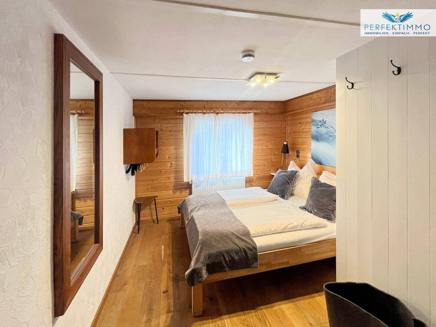 Helles Schlafzimmer mit Holzvertäfelung, Doppelbett und Holzboden.