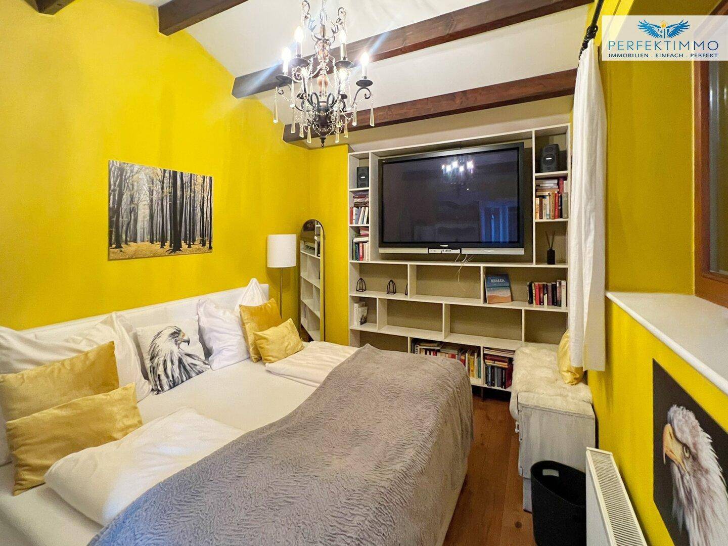 Farbenfrohes Schlafzimmer mit gelben Wänden, Doppelbett und Bücherregal.