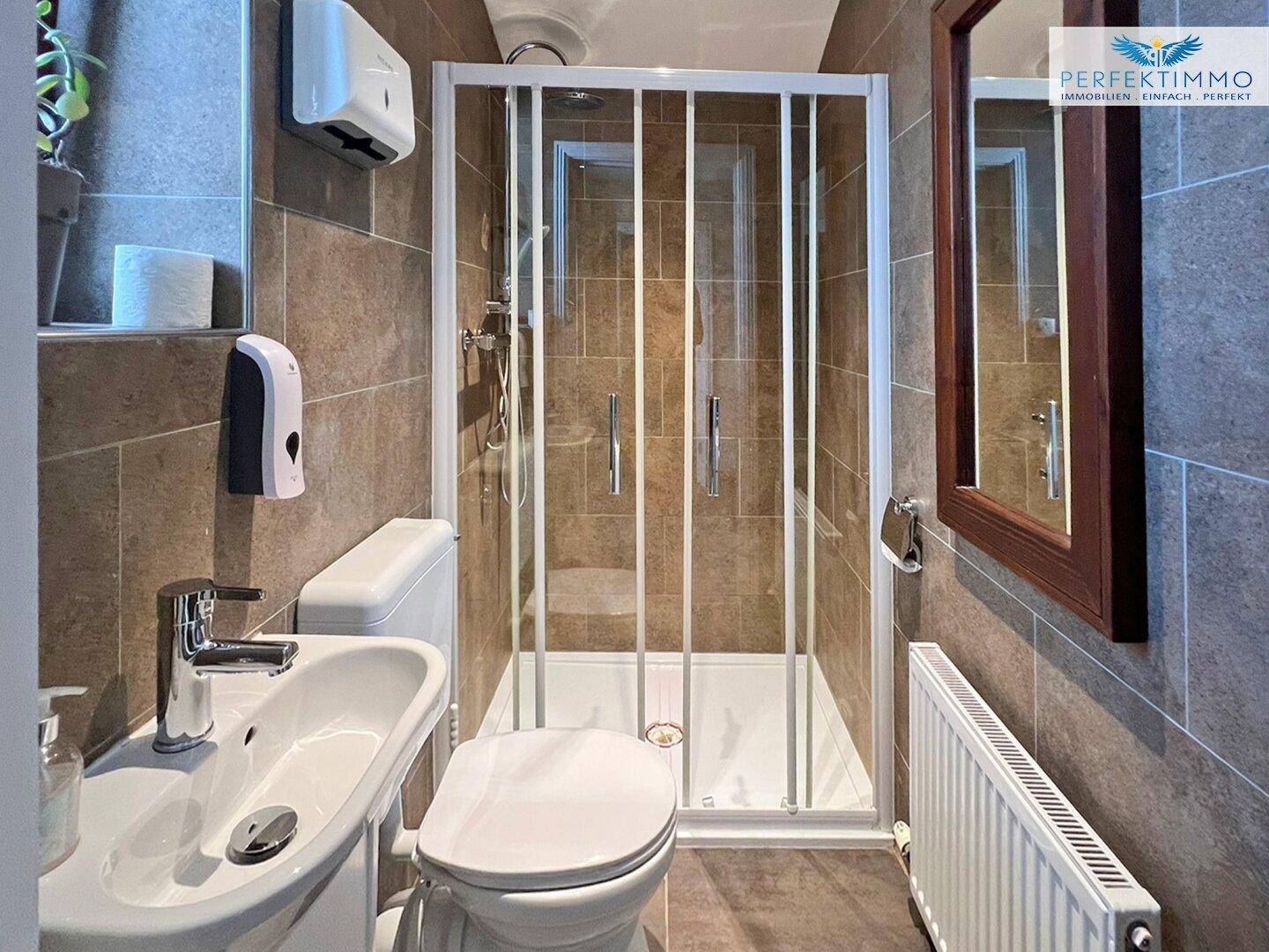 Modernes Badezimmer mit Duschkabine, WC und braunen Fliesen.